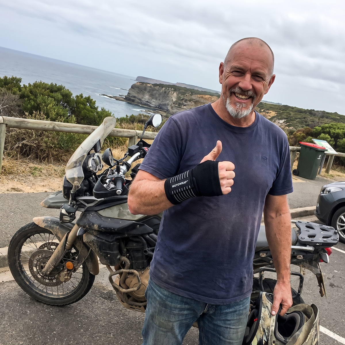 Rider at a coastal lookout giving a thumbs-up wearing a MotoWrap wrist support